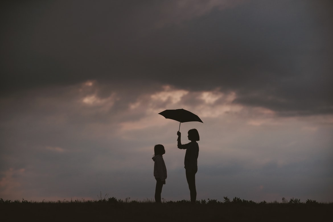 2 young girls stand under an umbrella.