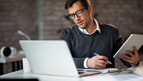 businessman wearing glasses looking at laptop and making notes