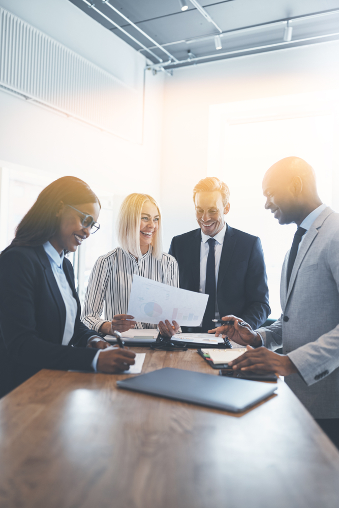 Smiling,Group,Of,Diverse,Businesspeople,Standing,Together,Around,A,Table