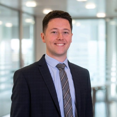Image of male wearing suit and tie smiling into camera in a modern office setting
