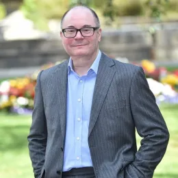 Male in suit no tie standing in garden smiling into camera