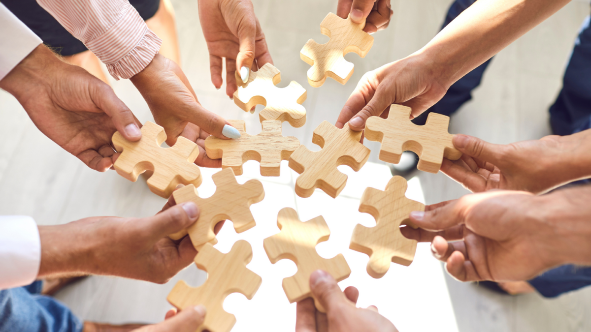 arms and hands wearing business atire each holding a piece of the jigsaw puzzle