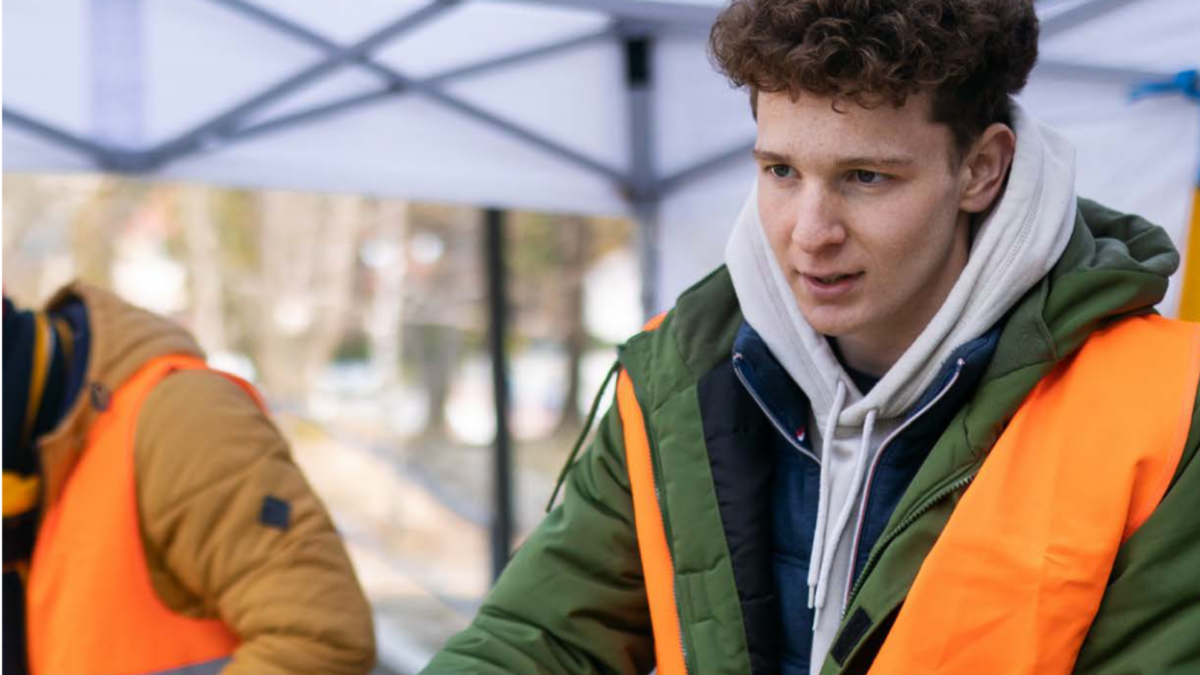 Image of a volunteer standing under a gazebo wearing a high viz handing out blankets