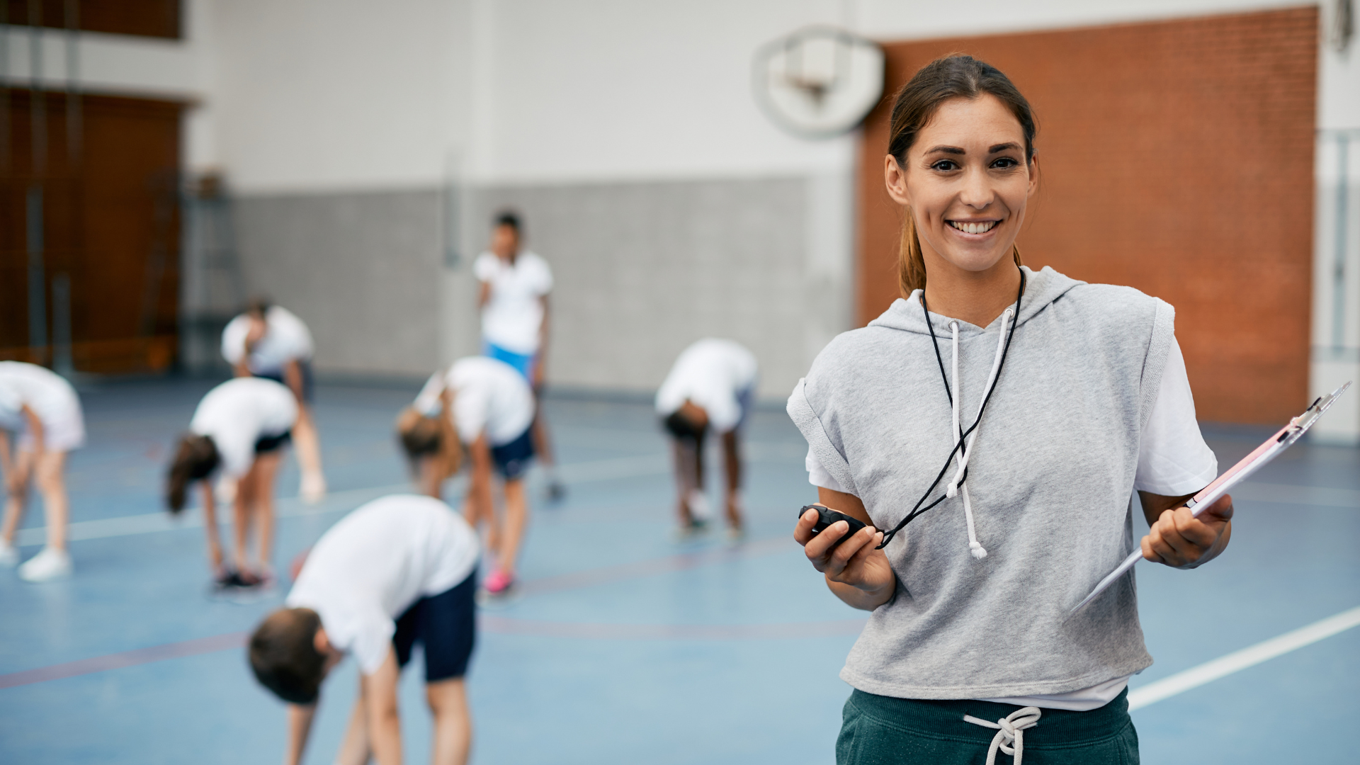 Female PE teacher holding stop watch and clipboard in a school gymnsasium