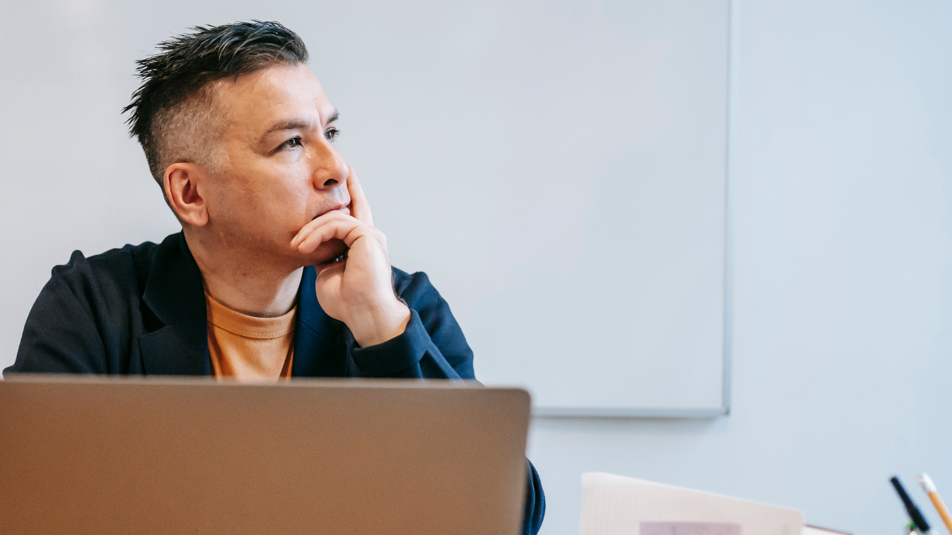 Image shows a man sitting at his laptop resting his head on his hands staring throughtfully into the distance