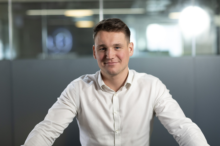 Young professional male in smart casual wear smiling into camera in an office setting