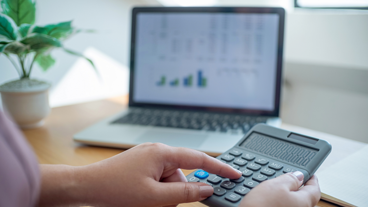 Image showing hands using a calculator with a laptop and paperwork and a pot plant in the background