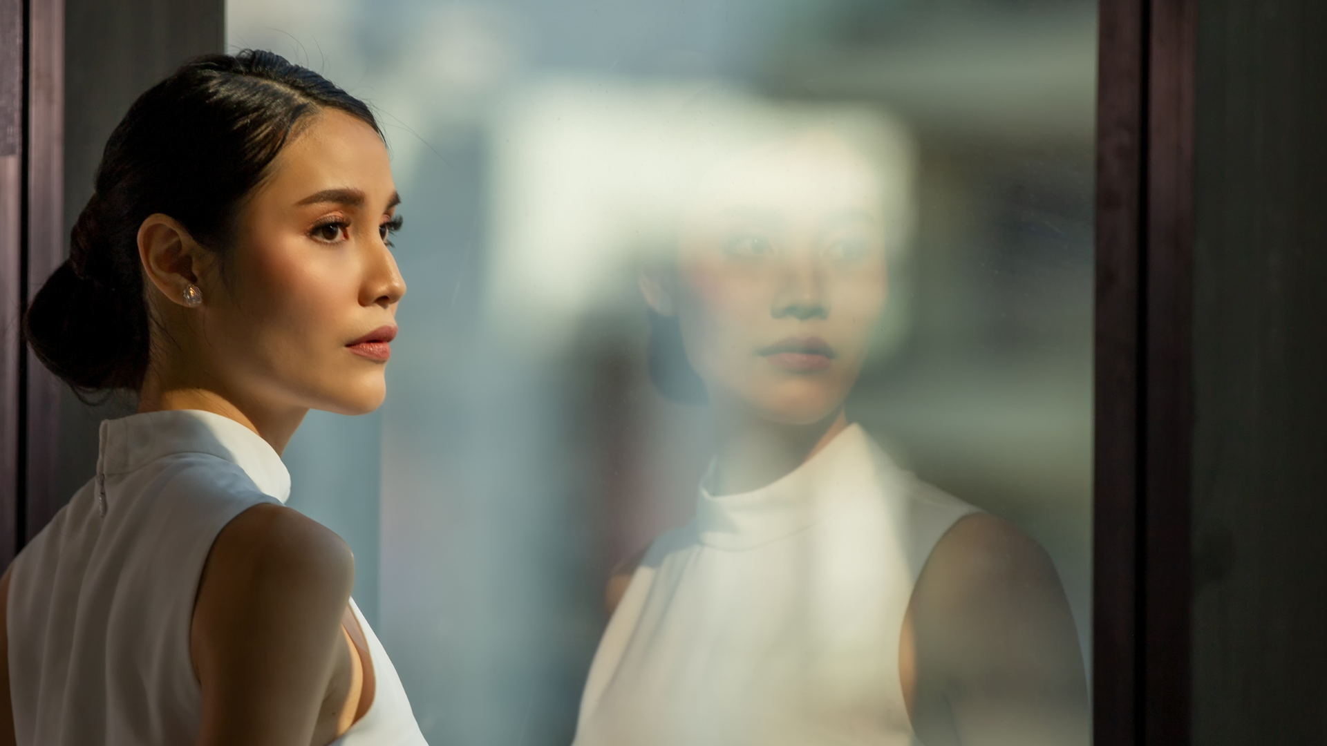 Female professional looking thoughtfuly out of a window with her reflection in the glass evident.