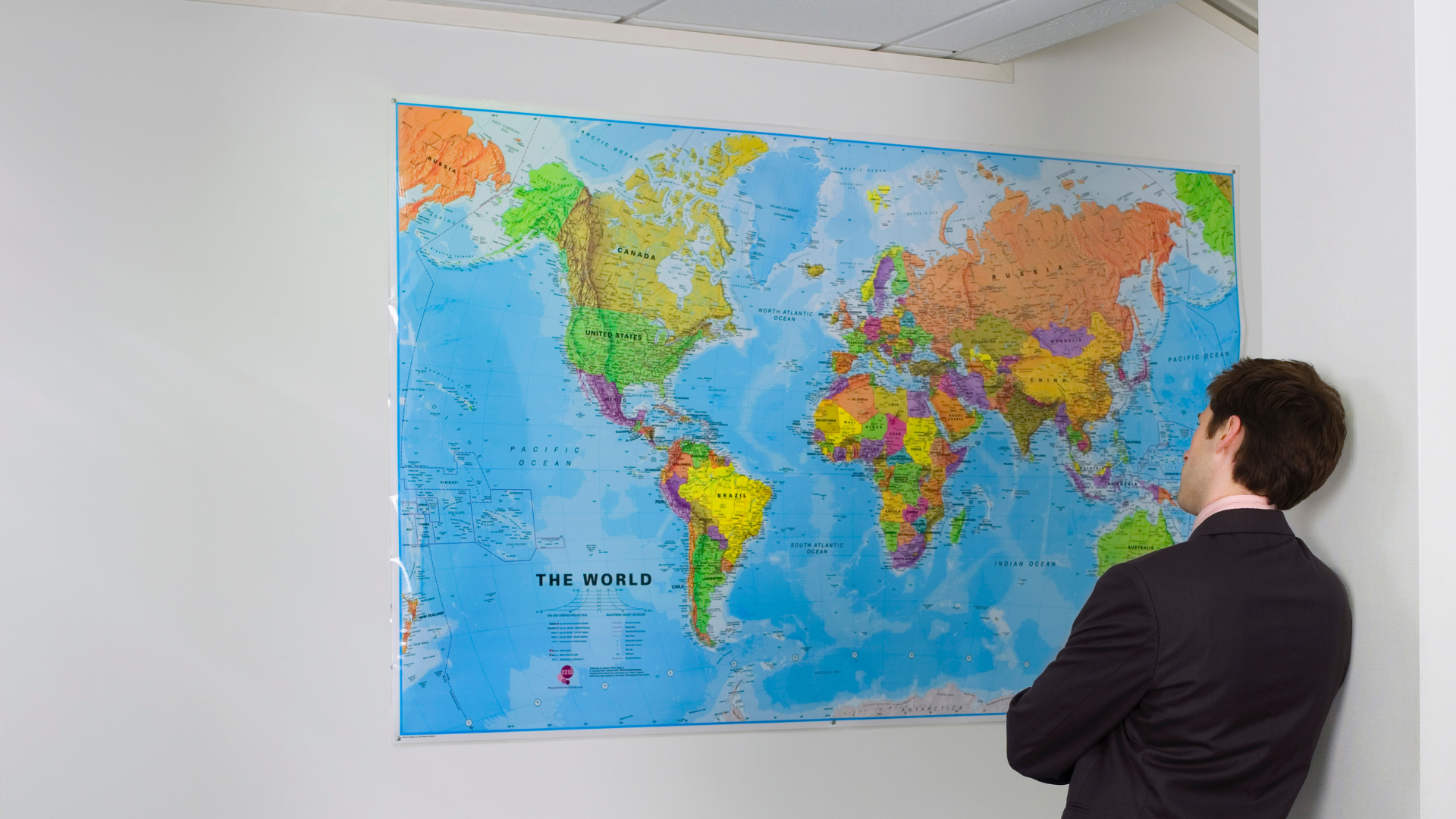 Business person standing in front of a map of the world looking thoughful